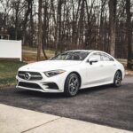 A sleek white Mercedes-Benz sedan parked on a driveway surrounded by a wooded area.